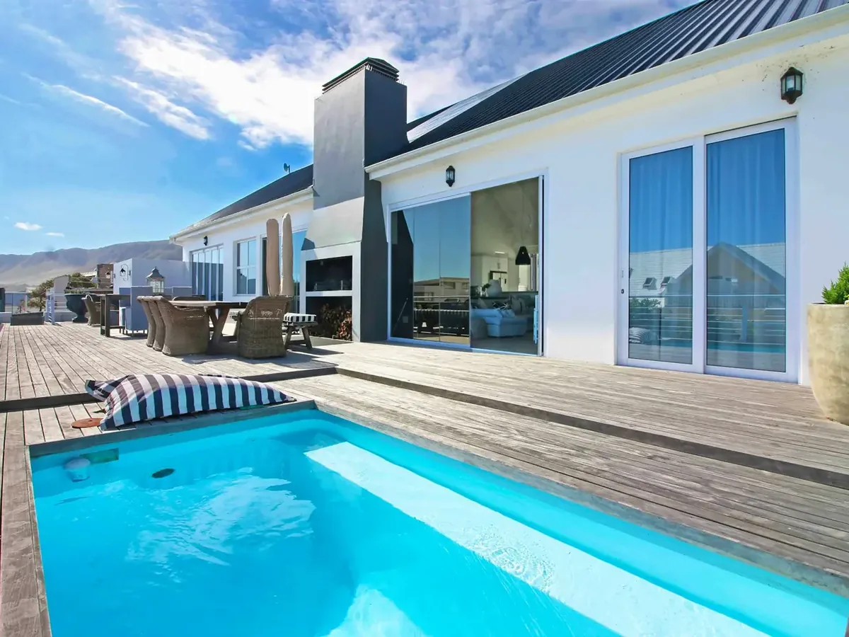 The pool terrace and sea-facing living areas of Voelklip Villa, a five-bedroom luxury villa a hundred metres from the cliff path in Voelklip, Hermanus